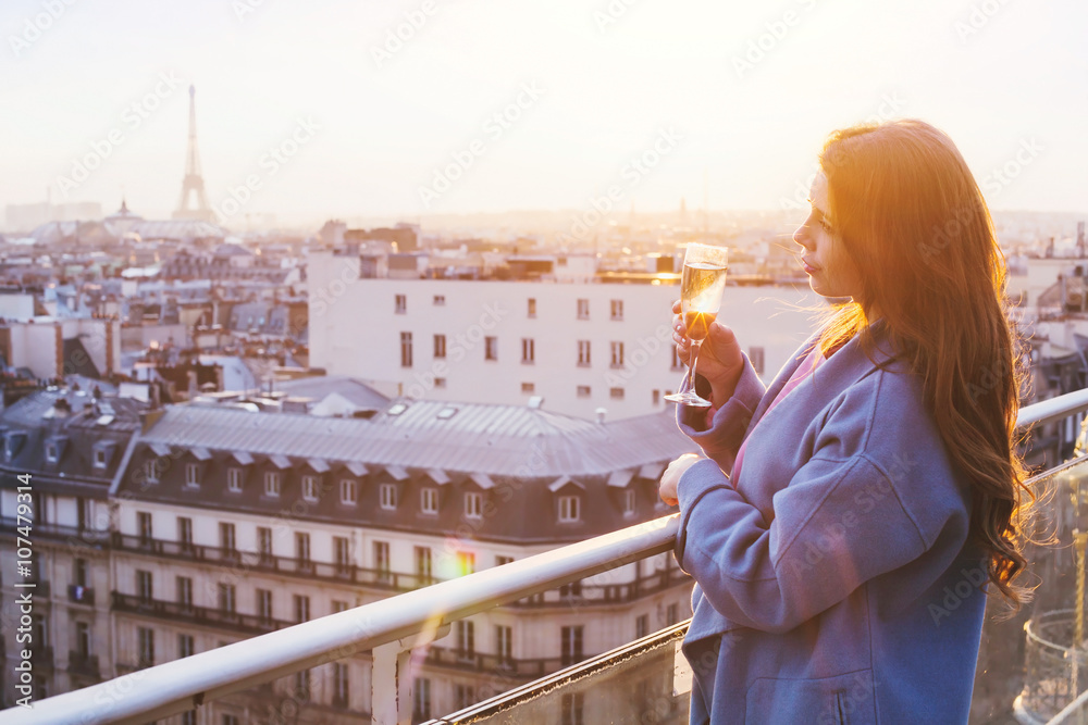 Fototapeta premium woman enjoying panoramic view of Paris and Eiffel tower at sunset, holding glass of wine or champagne in rooftop luxury restaurant