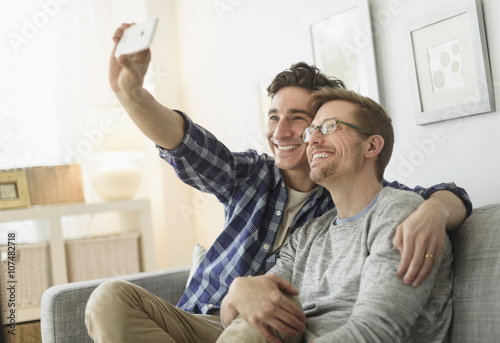 Caucasian gay couple taking selfie on sofa