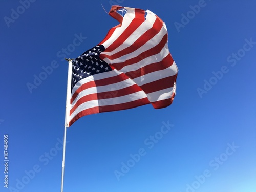 A torn American flag flying against a blue sky. 