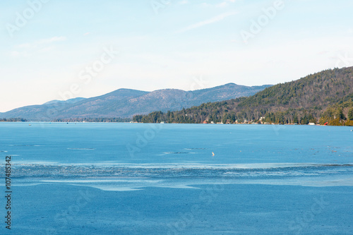 Color DSLR stock image of a frozen Lake George  with lake houses on the shore and Adirondack Mountains in background. Horizontal with copy space for text  