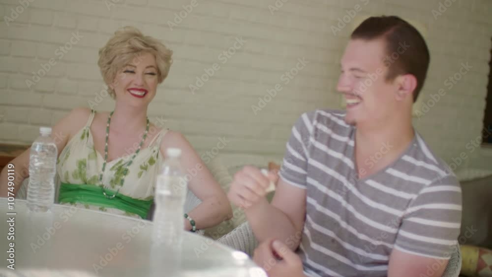 Group of four good-looking people laugh and toast with water bottles on a sunny indoor porch. Focus changes to different people during clip, with end focus on bottles. Hand held camera Group of four good-looking people laugh and toast with water bottles on a sunny indoor porch. Focus changes to different people during clip, with end focus on bottles. Hand held camera