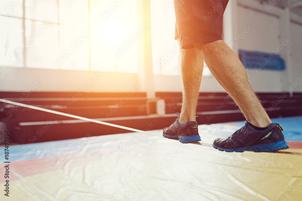 Fototapeta premium Man slacklining walking and balancing on a rope, slackline in a sports hall
