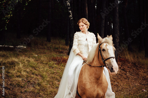 beautiful stylish gorgeous young bride sitting on a brown horse in forest