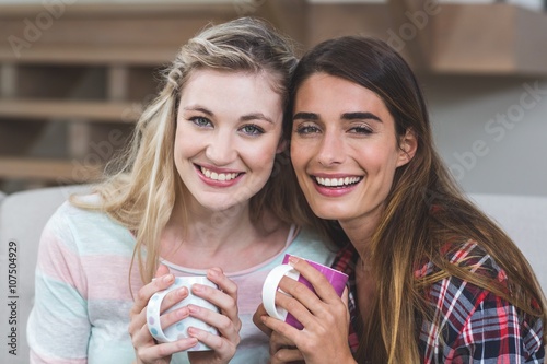 Two beautiful women sitting side by side with a mug of coffee