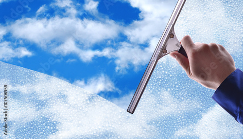 Employee cleaning a glass with rain drops and blue sky