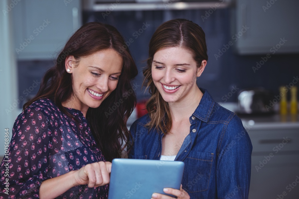 Two beautiful women using digital tablet in kitchen Two beautiful women using digital tablet in kitchen
