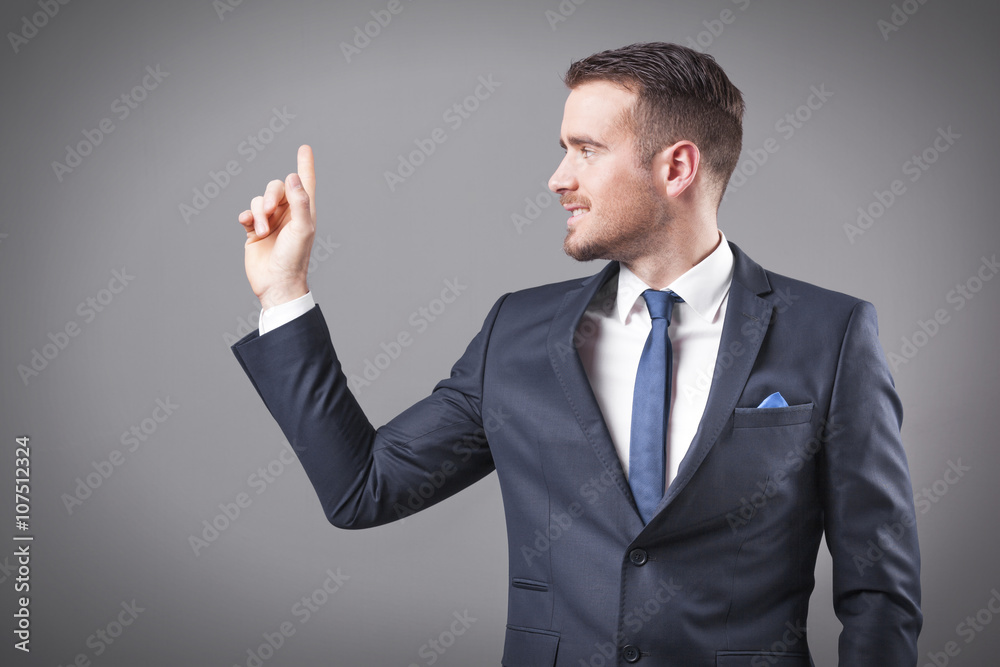 Handsome smiling business man pointing at copy space on grey bac Handsome smiling business man pointing at copy space on grey bac