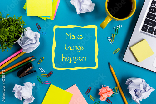 Make things happen. Office table desk with supplies, white blank note pad, cup, pen, pc, crumpled paper, flower on blue background. Top view