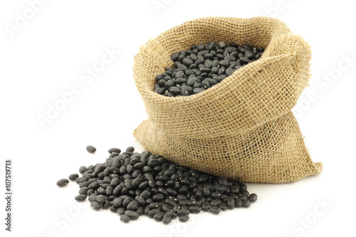 dried black beans in a burlap bag on a white background