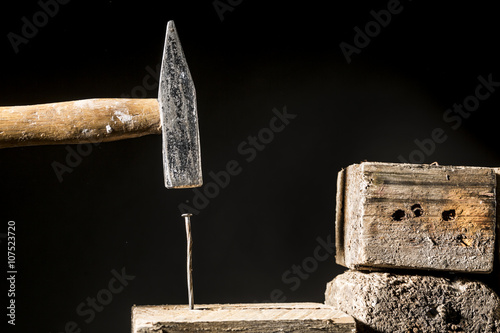 Martello che pianta un chiodo sopra del legno - sfondo nero photo