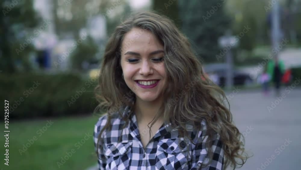 The young woman walk, turn and smile by street background. Camera follow behind The young woman walk, turn and smile by street background. Camera follow behind