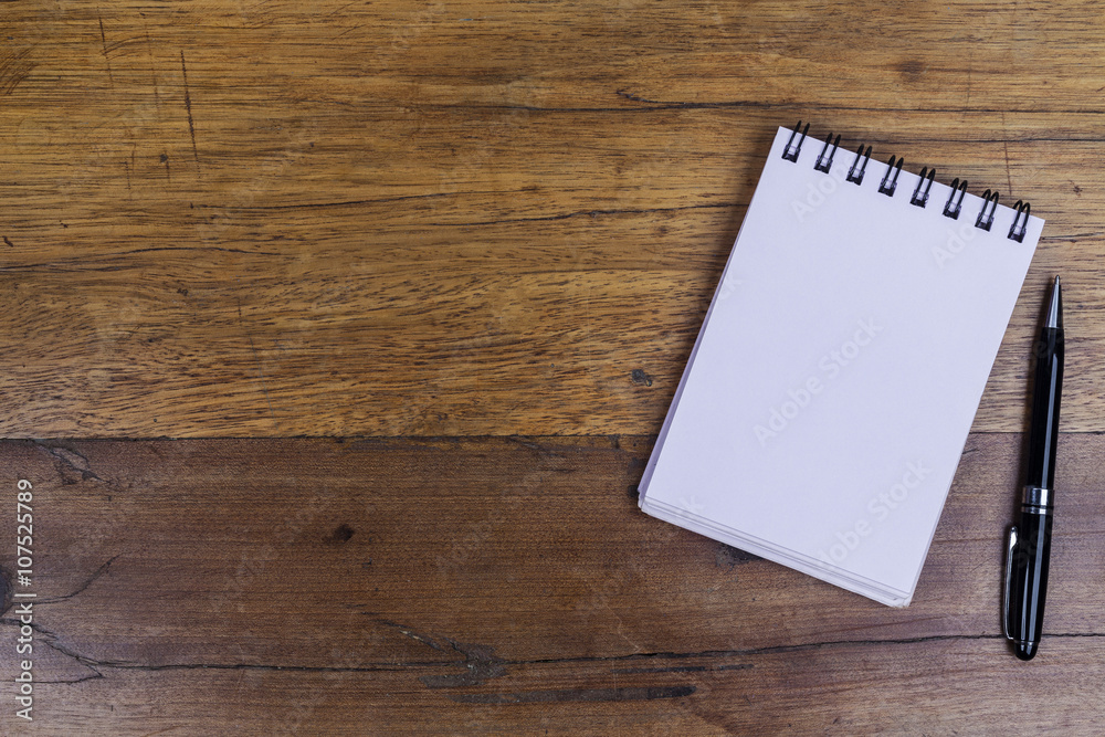 White sheets notebook with spiral on right side of the wooden dark brown table with black pen aside from above White sheets notebook with spiral on right side of the wooden dark brown table with black pen aside from above