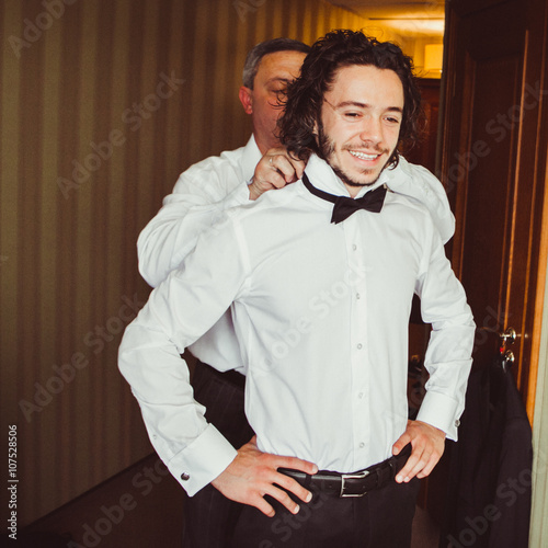 Groom's father helping get ready for wedding, putting on bowtie
