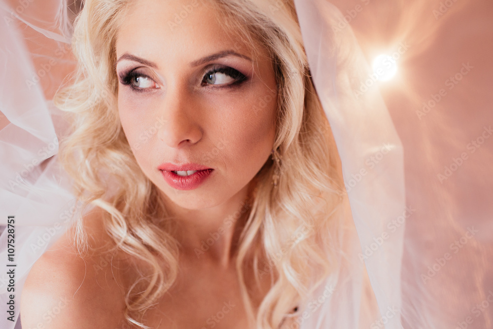 Beautiful emotional blonde bride posing under veil, face closeup