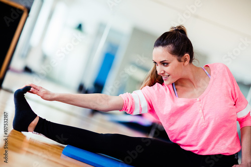 Young brunette european white caucasian girl exercising alone in gym with wooden floor doing yoga, pilates and fitness exercises