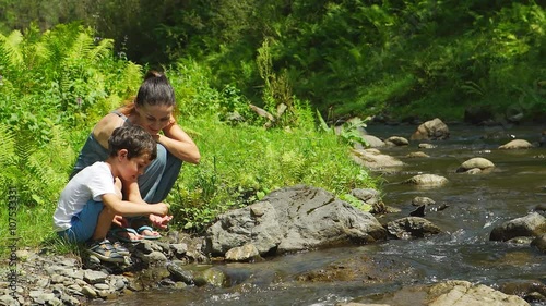 Mother with her son are sitting near a stream