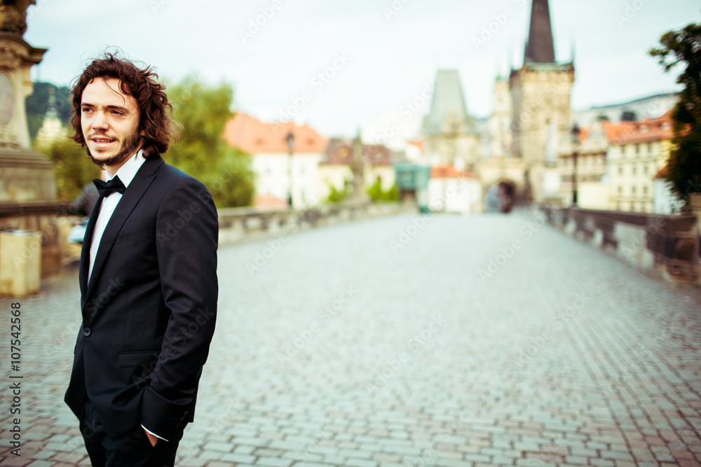 Handsome bearded stylish groom in suit posing on bridge in Pragu Handsome bearded stylish groom in suit posing on bridge in Pragu