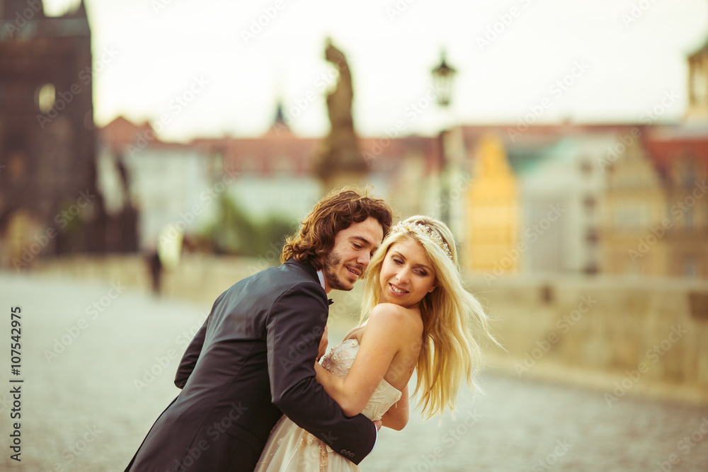 Fototapeta premium Romantic newlywed couple on honeymoon, hugging on bridge in Prag
