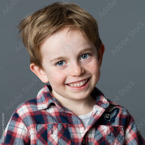 close up portrait of a red hair 5-year old preschooler with freckles giggling for childhood and wellbeing, grey background studio.