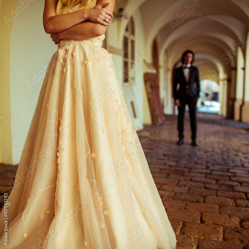 Beautiful blonde bride posing near buildng, groom in background photo