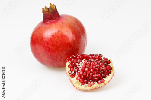 Fresh red pomegranate fruit, with one peeled piece, on white background.