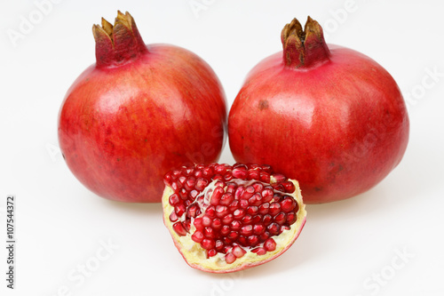 Two fresh red pomegranate fruits, with one peeled piece, on white background.