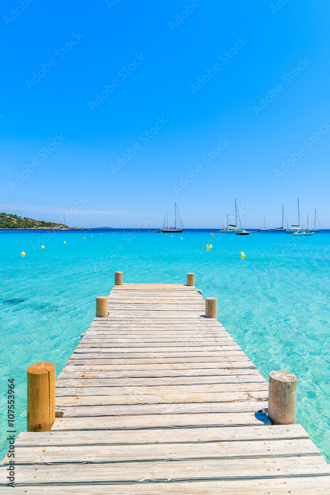 Wooden pier and crystal clear turquoise sea water on Santa Giulia beach, Corsica island, France