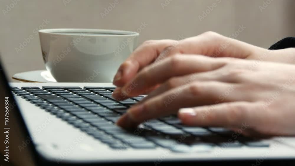 Femine hands typing on the keyboard of a laptop and taking cup with tea or coffee Femine hands typing on the keyboard of a laptop and taking cup with tea or coffee