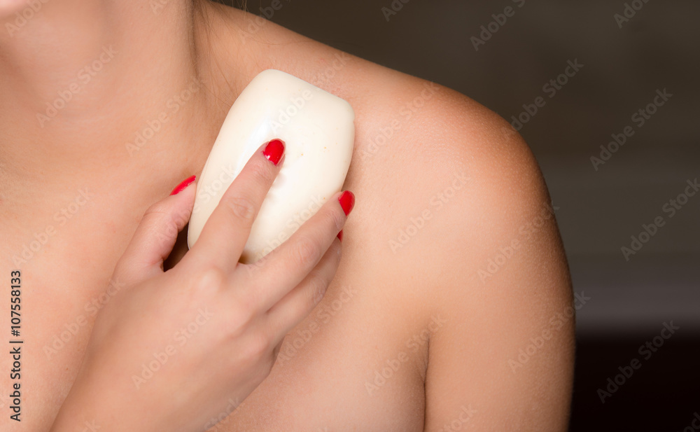 Closeup young womans bare skin shoulders and upper chest, rubbing bar of soap on body Closeup young womans bare skin shoulders and upper chest, rubbing bar of soap on body