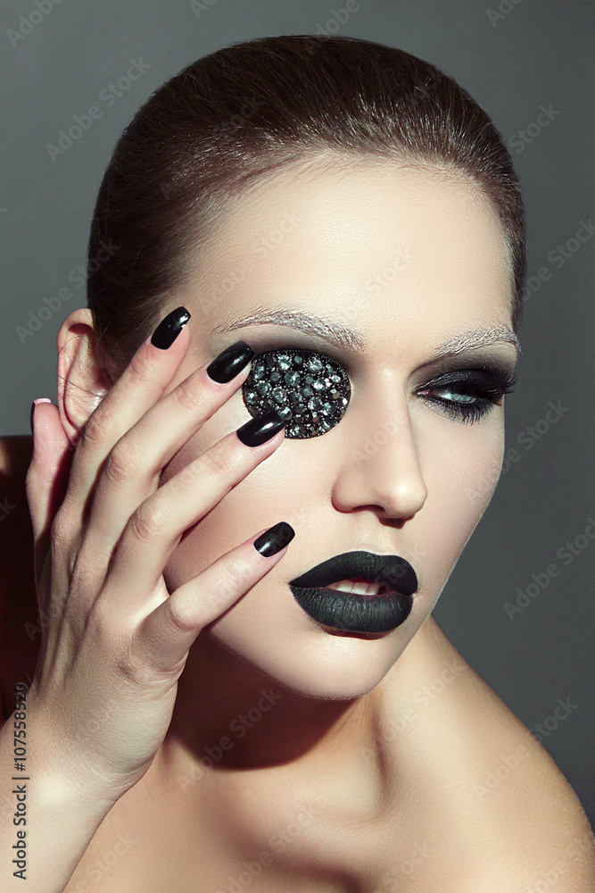 The girl's face with a decoration of rhinestones on the eye. Black makeup.  Black velvet lipstick. Smooth black hair. Pirate. Stock Photo