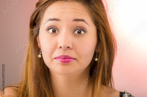 Headshot young pretty hispanic woman brunette with red lipstick, looking mildly startled, pink background