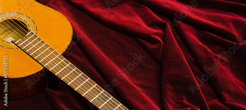Classical nylon guitar lying on red velvet textile, artistic instrument presentation
