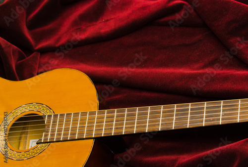 Classical nylon guitar lying on red velvet textile, artistic instrument presentation