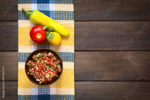 Traditional Chilean Pebre sauce made of tomato, onion, aji verde (small green hot pepper), lemon juice and coriander leaves, photographed on wood with natural light photo