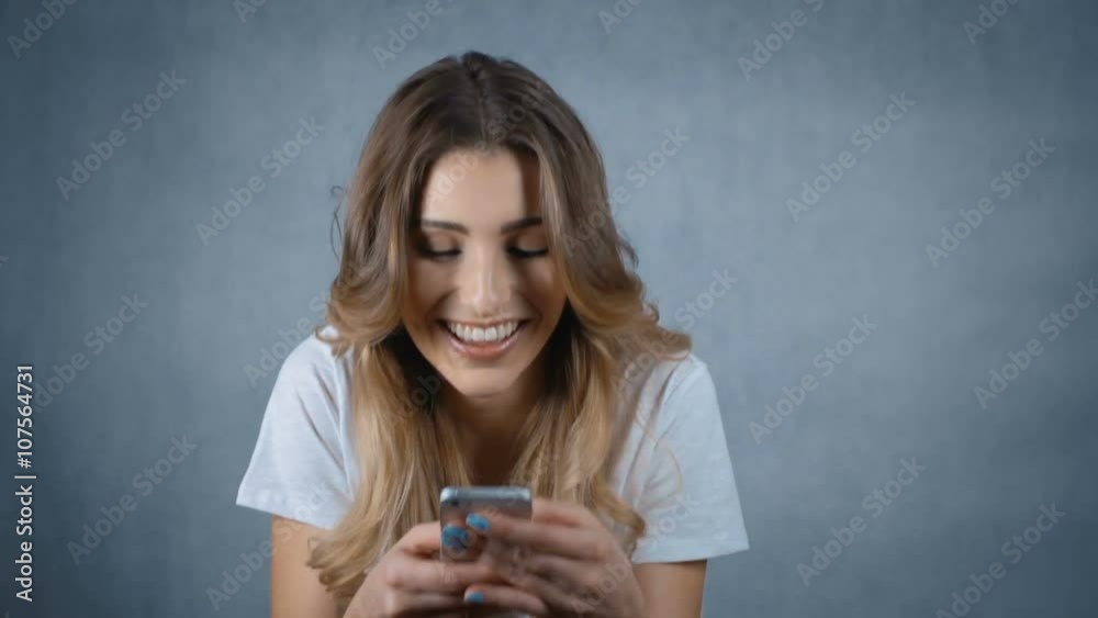 Cheerful young woman holding mobile phone and smiling over grey background. Cheerful young woman holding mobile phone and smiling over grey background.
