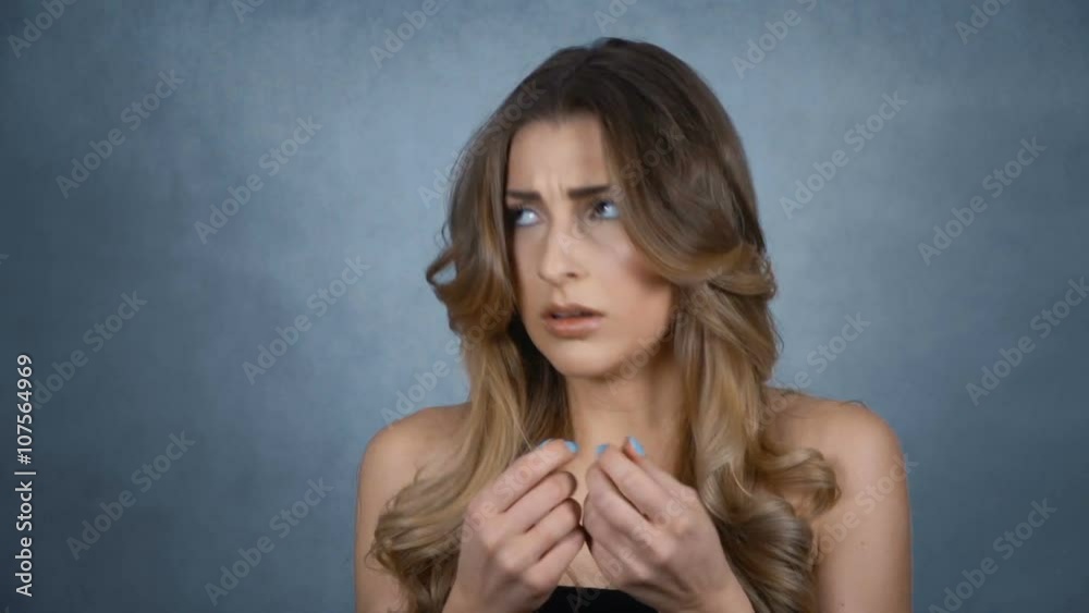 Young stressed woman biting her nails over grey background.