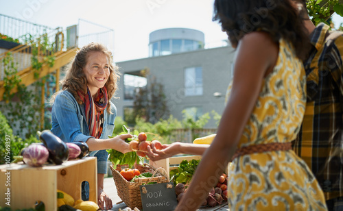 Friendly woman tending an organic vegetable stall at a farmer's market and selling fresh vegetables from the rooftop garden photo