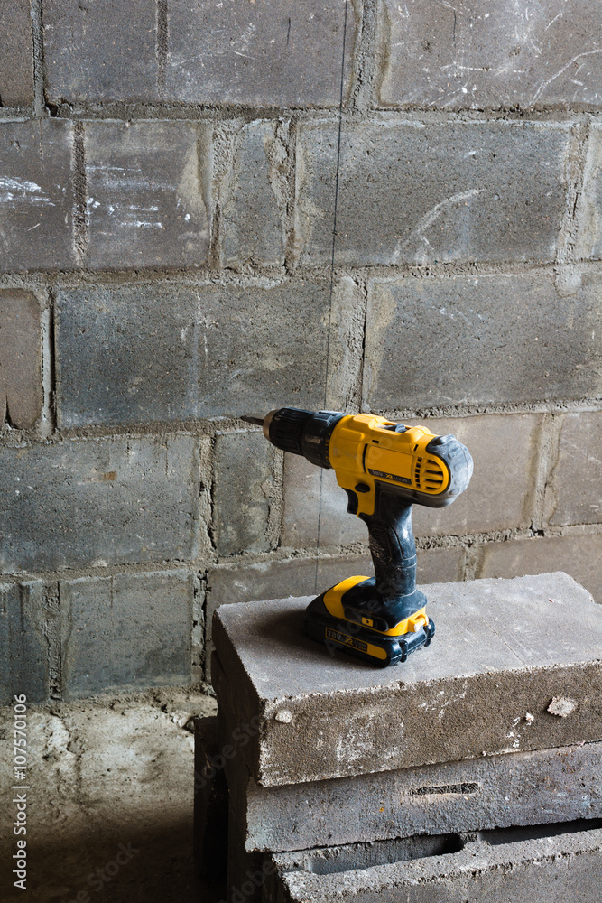 Electric drill against the backdrop of the walls of foam concrete. Unfinished apartment interior.