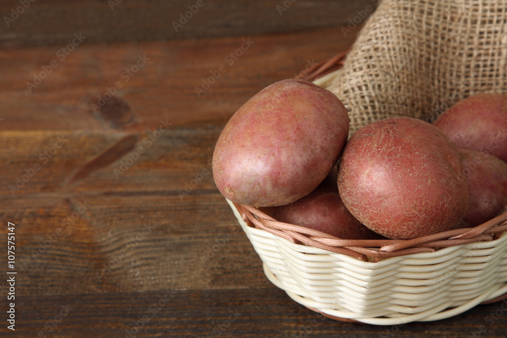 red potatoes on burlap in a wooden wicker basket on wooden brown background
