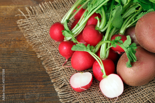 red potatoes on burlap with sliced radishes on wooden brown background