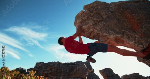 Bouldering rock climber hanging beneath extreme overhang against blue sky