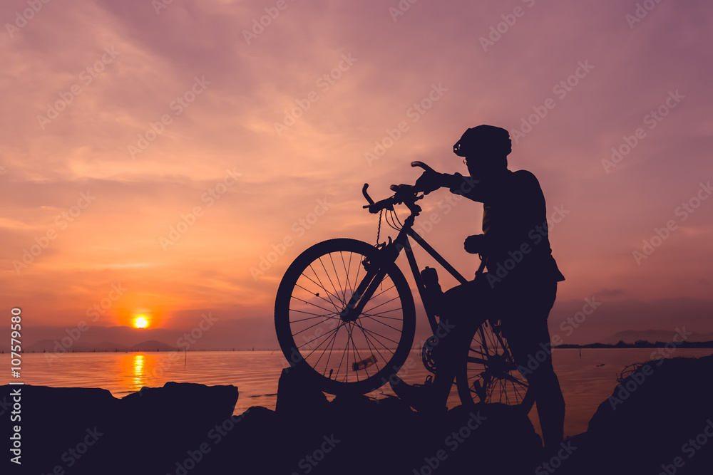 Obraz premium Healthy lifestyle. Silhouette of bicyclist standing with bike at seaside.