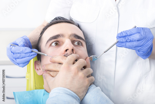 Frightened man at dentist office covered mouth with hands.