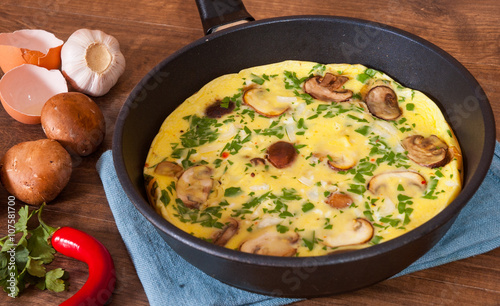 omelet with mushrooms in a frying pan on wooden table