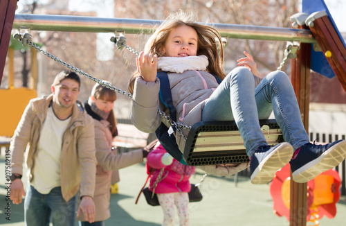 Parents watching little daughters swinging.