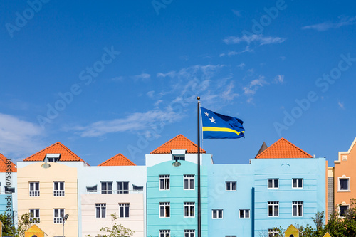 Bild auf Leinwand Curacao Flag by Blue Buildings under Blue Skies