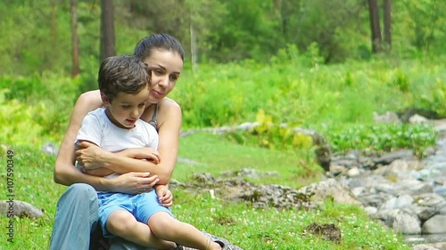 Mother hugs her son near a stream