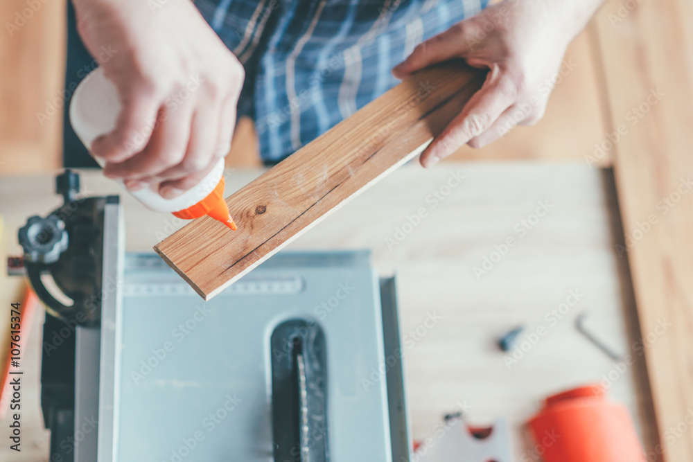 Carpenter applied glue on wooden board in his workshop.