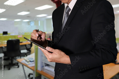 Business Man using Tablet device on blurred abstract in the office background as Working Concept.