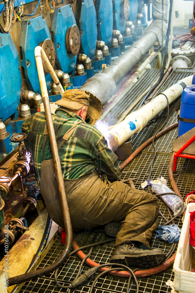 Welder during the repair welding of the pipeline in the engine room of the ship - obrazy, fototapety, plakaty 